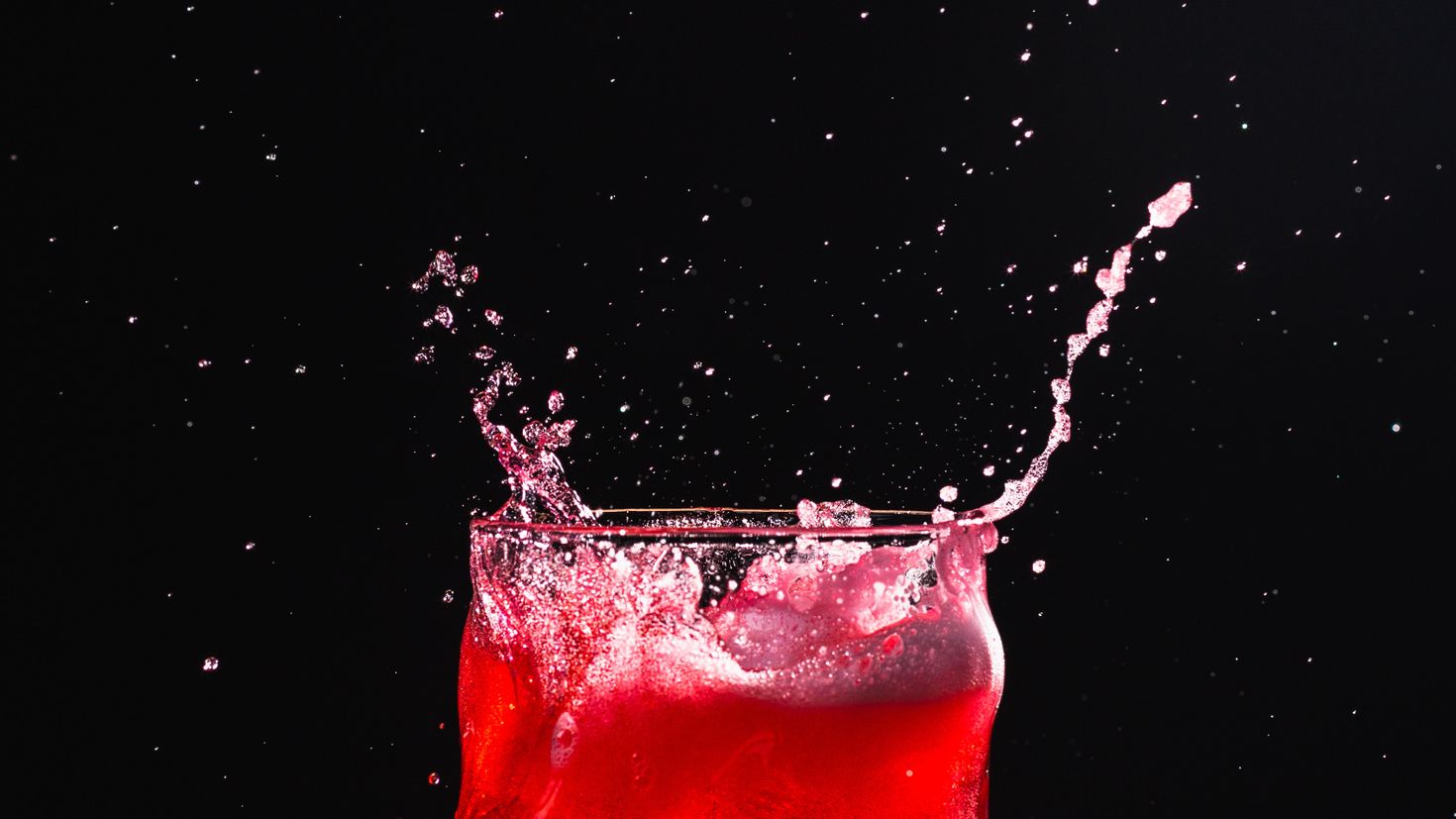 В воду красный из воды черный. Брызги напитка. Напитки со льдом. Стакан воды на Красном фоне. Газировка в стакане на темном фоне.