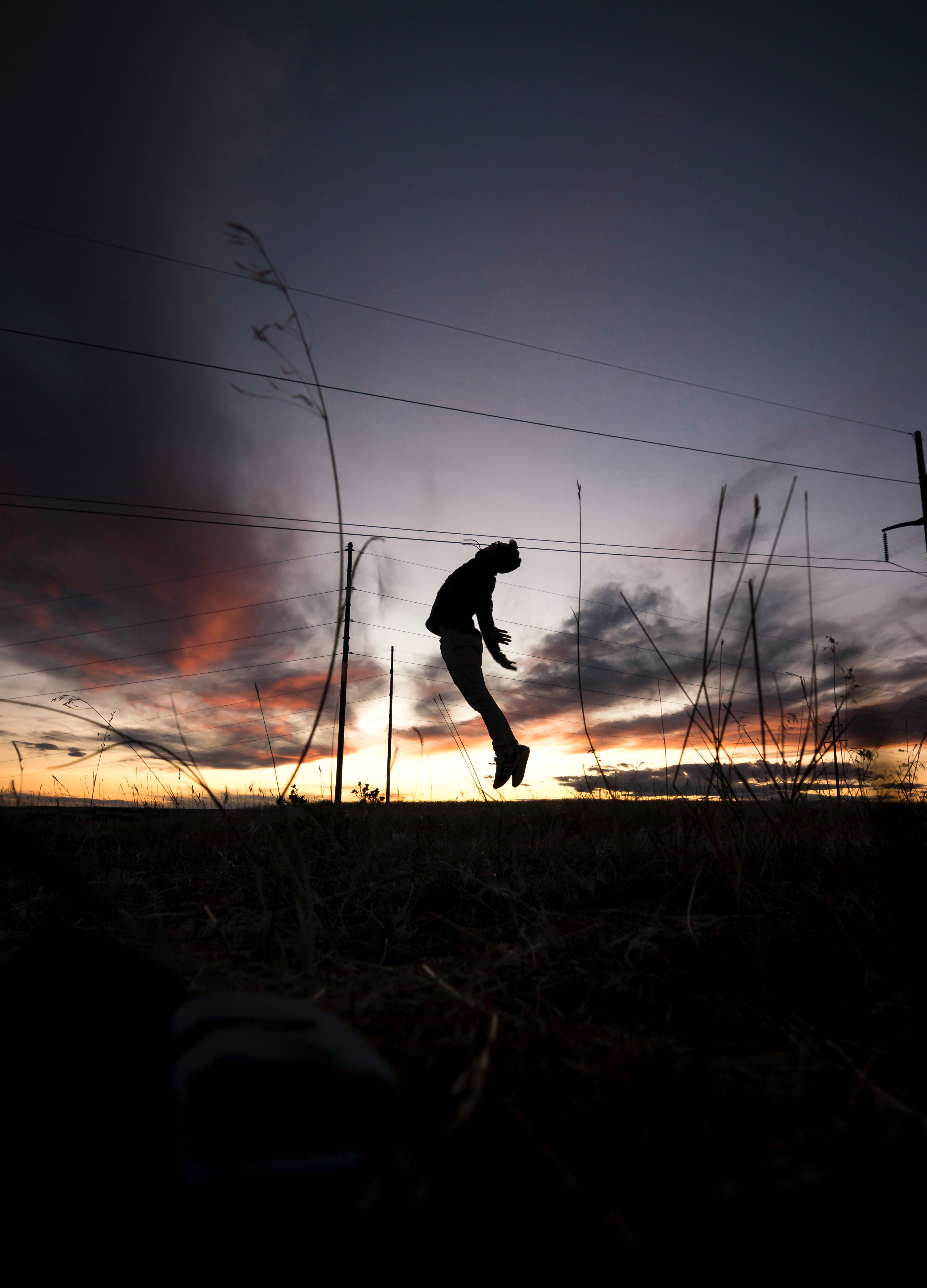 Download mobile wallpaper Bounce, Grass, Jump, Person, Sunset, Silhouette, Human, Dark for free.